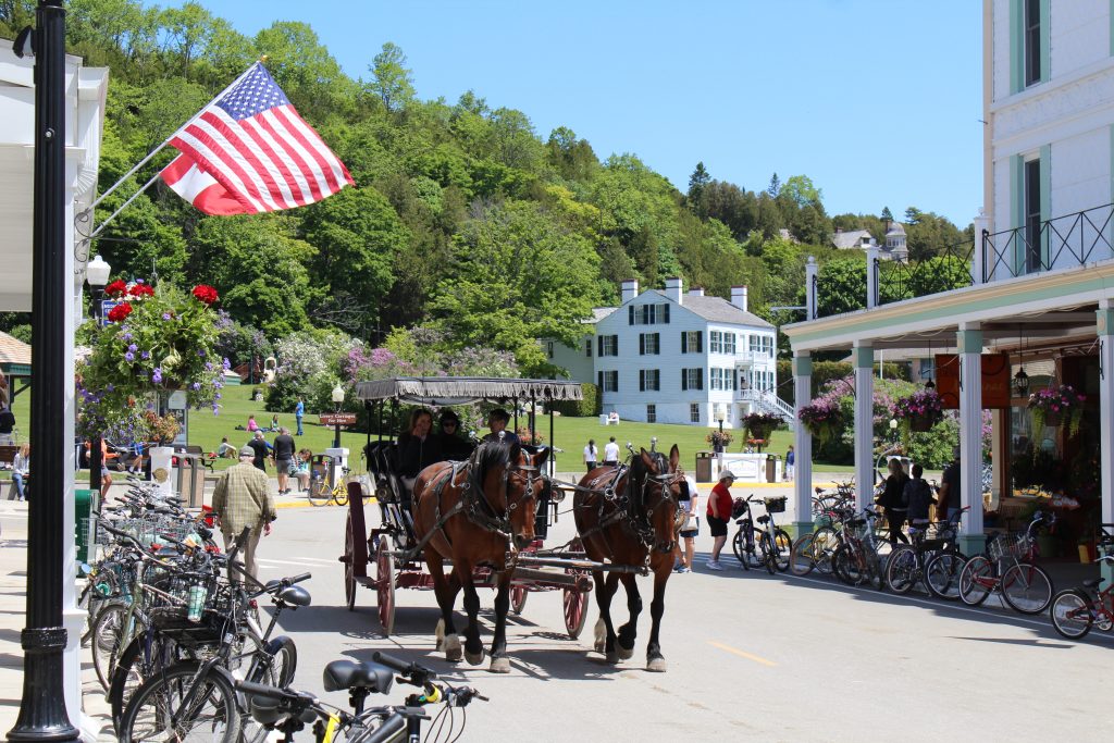 A two-horse carriage carries passengers past the Victorian buildings of Mackinac Island's main thoroughfare.